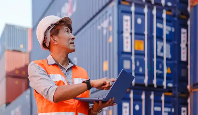 Logistics worker inspecting shipping containers with a laptop